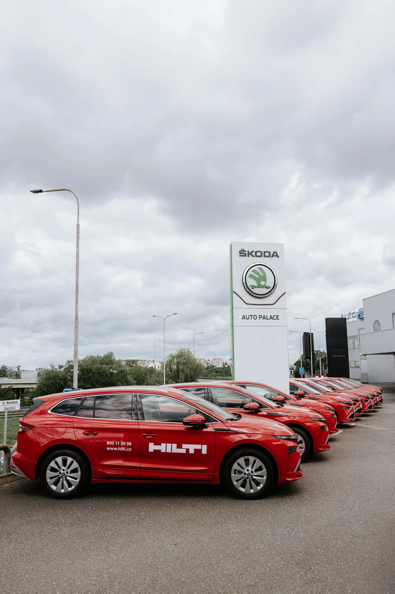 Řada červených elektromobilů Škoda Enyaq v barvách Hilti před pylonem AutoPalace Spořilov