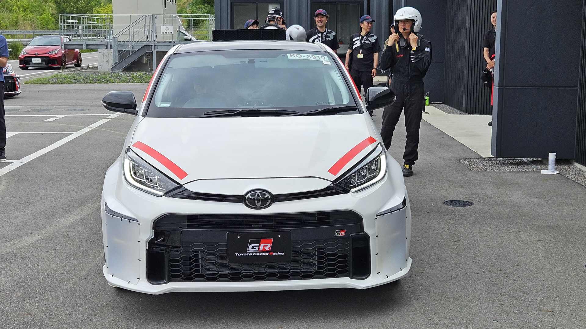 Prototyp Toyota se středovým motorem na testovacím polygonu, kolem stojí tým v přilbách