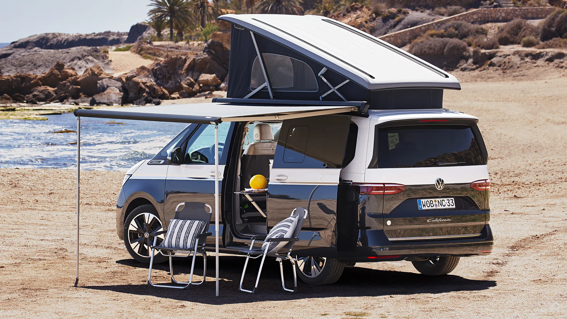 Volkswagen California Ocean s vyklopenou střechou a markýzou v kempovém uspořádání u pláže