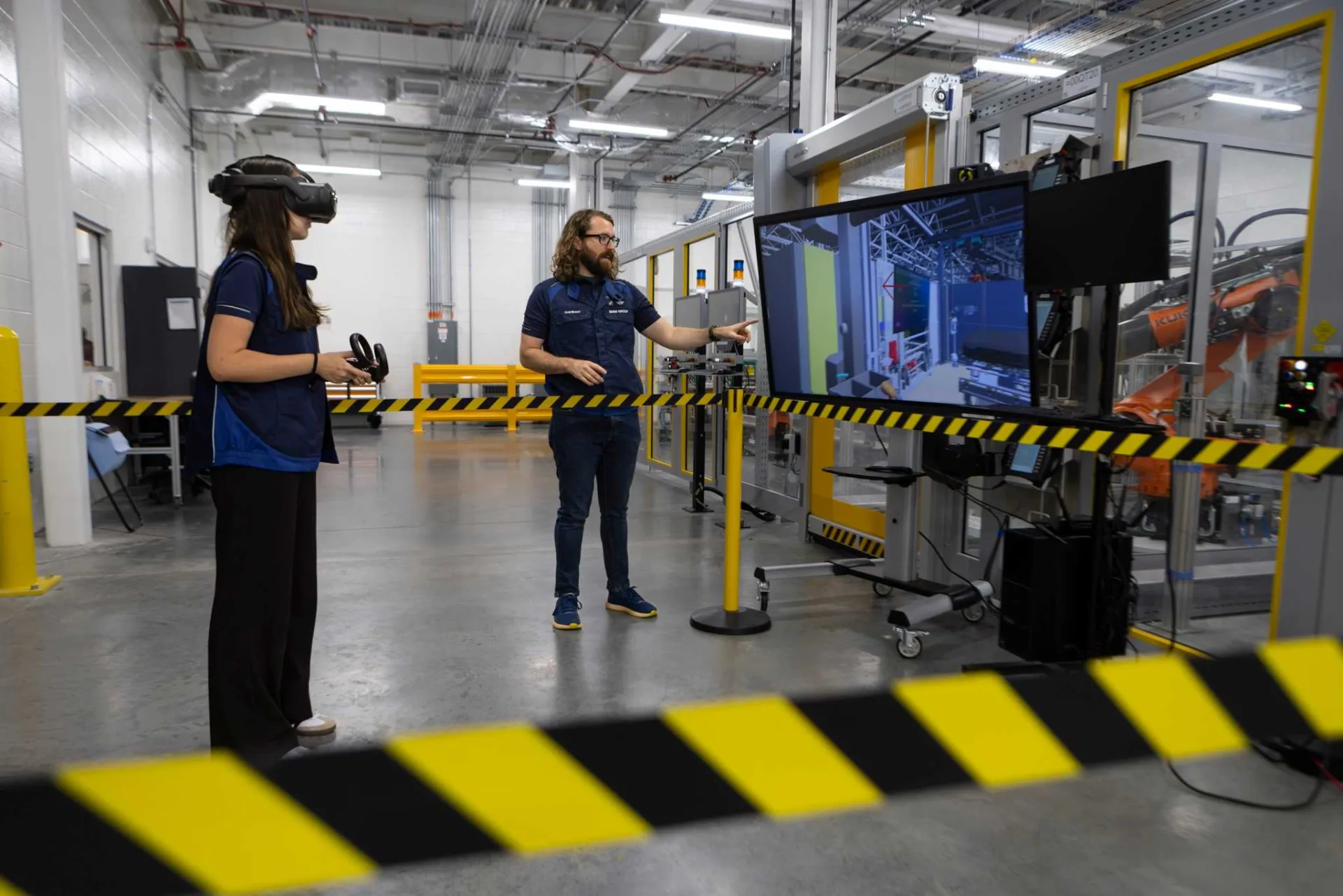 Školení ve virtuální realitě v továrně BMW Group ve Woodruffu, pracovnice s VR brýlemi a instruktor u obrazovky s digitálním dvojčetem linky