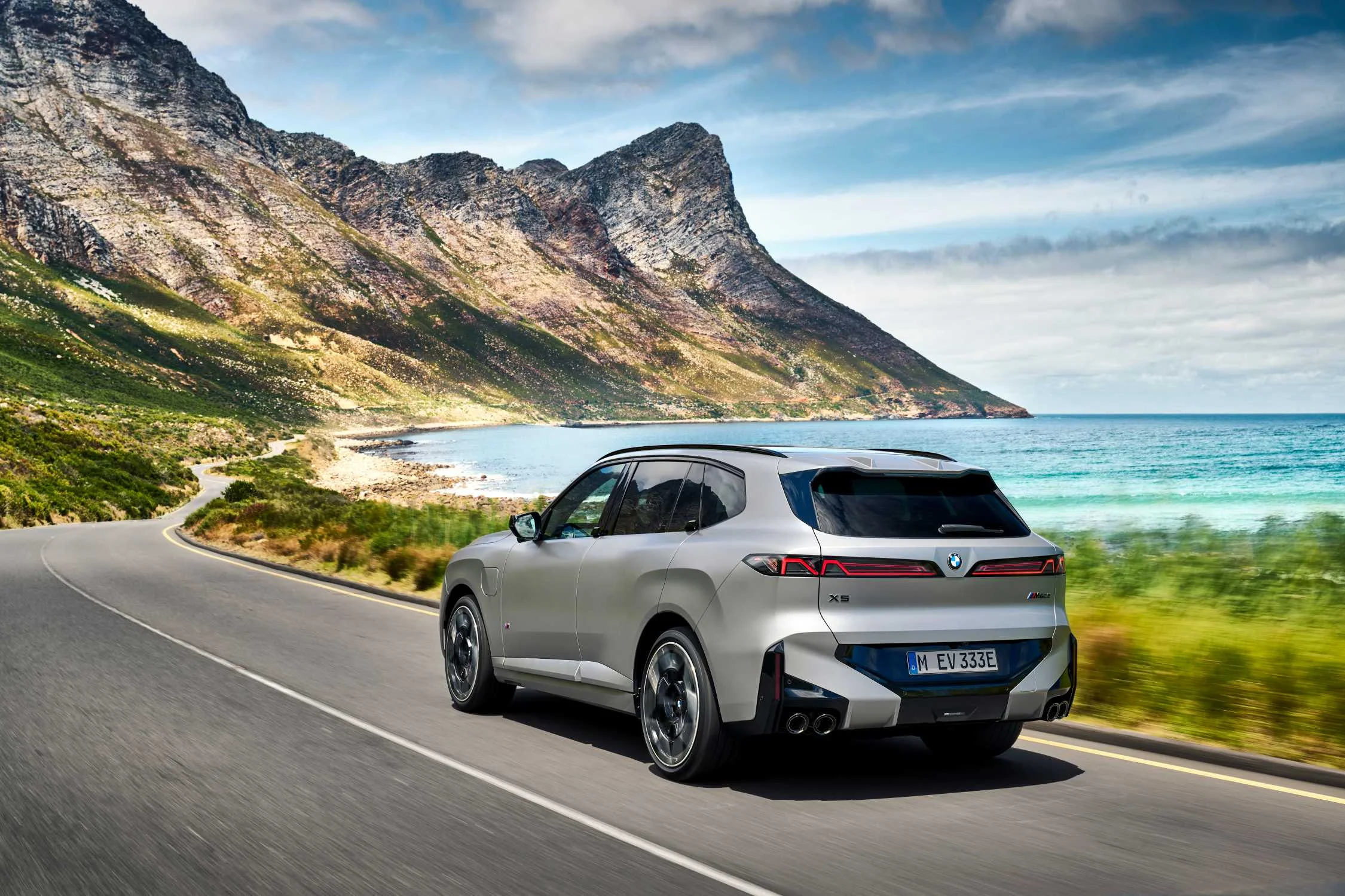 BMW X5 M60e xDrive ve stříbrné barvě na pobřežní silnici