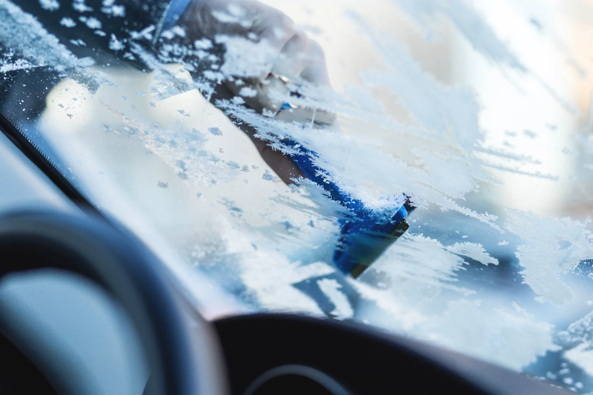 Ruka odstraňuje škrabkou námrazu z čelního skla automobilu
