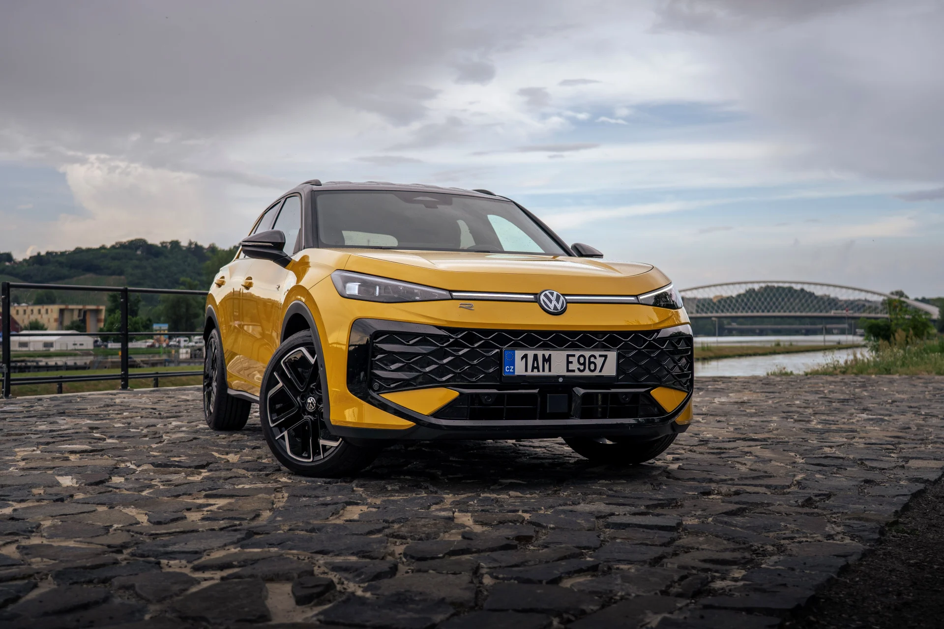 Žlutý Volkswagen T-Roc nové generace zepředu na dlážděném nábřeží u řeky