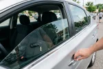 Klíče od auta s dálkovým ovladačem leží na sedadle řidiče uvnitř zamčeného vozu, ruka drží kliku dveří zvenku