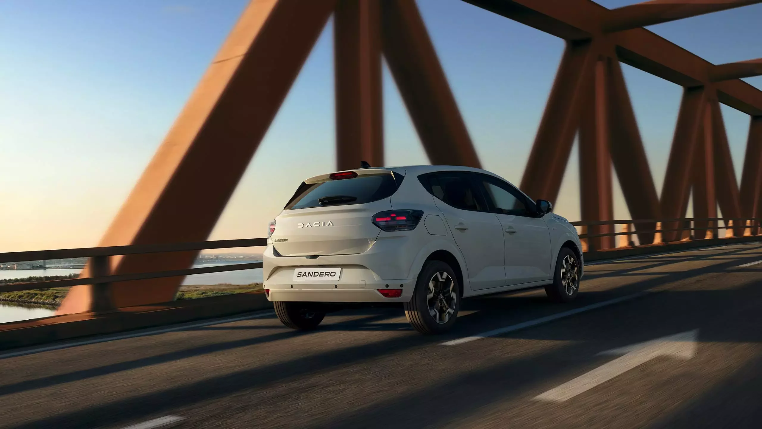 Bílá Dacia Sandero při jízdě po mostě