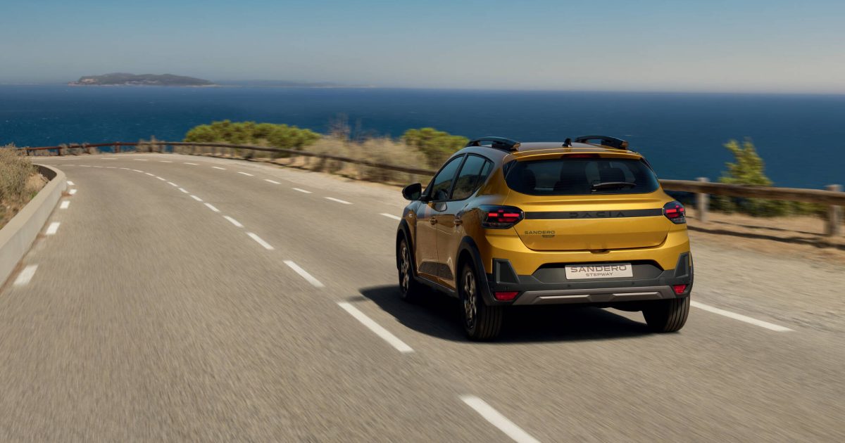Dacia Sandero Stepway Hybrid 155 v žluté barvě na pobřežní silnici, pohled zezadu