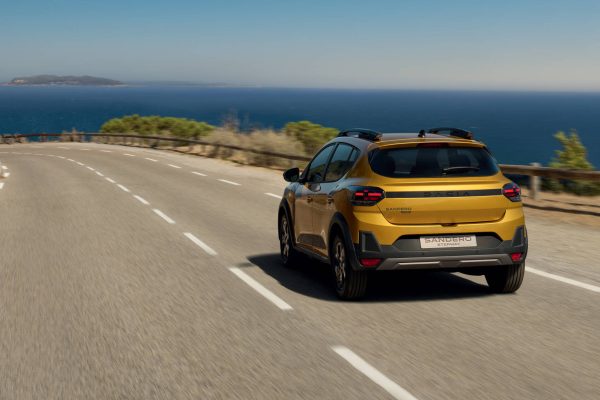 Dacia Sandero Stepway Hybrid 155 v žluté barvě na pobřežní silnici, pohled zezadu