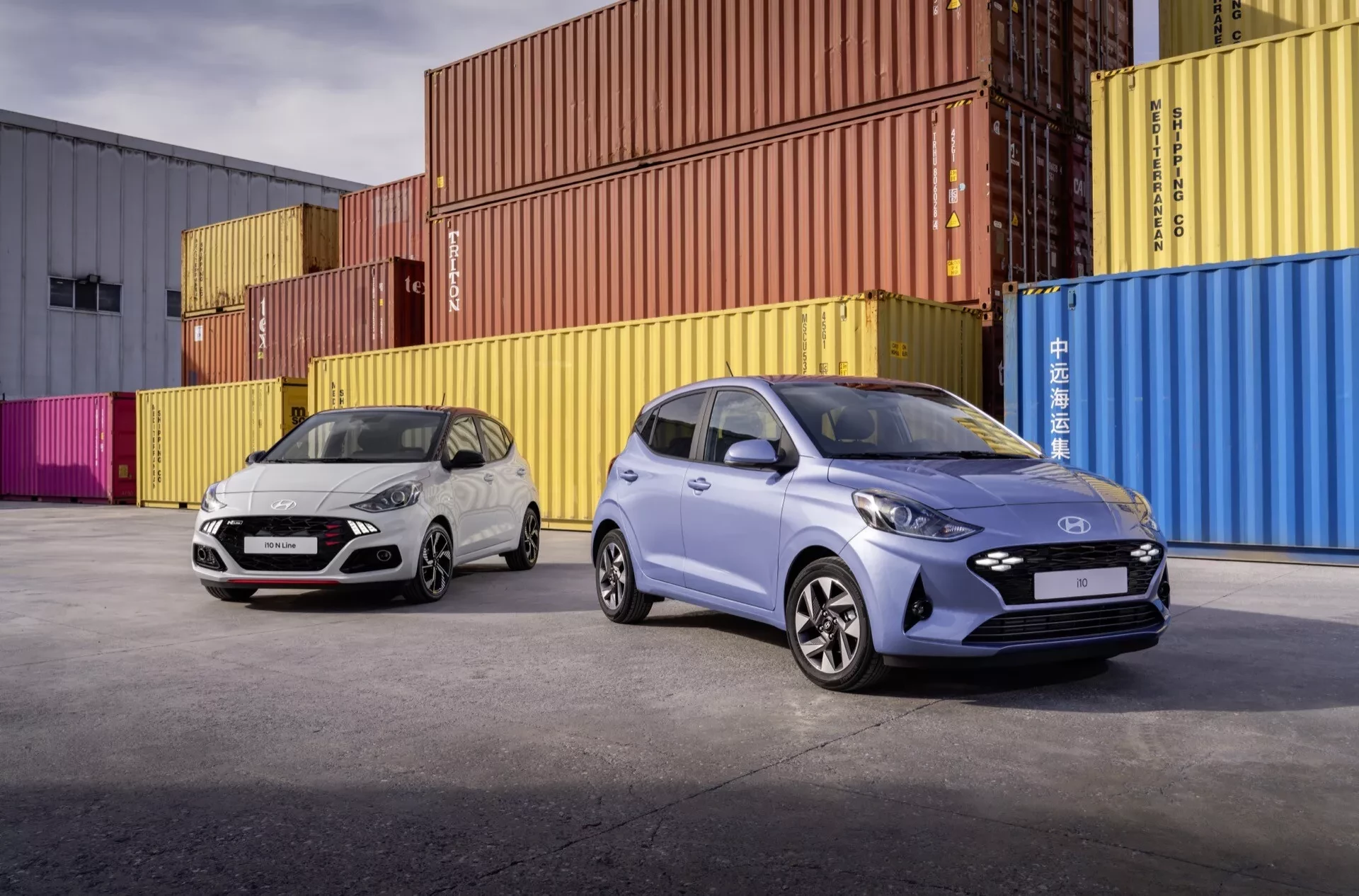Dva vozy Hyundai i10 současné generace před barevnými kontejnery