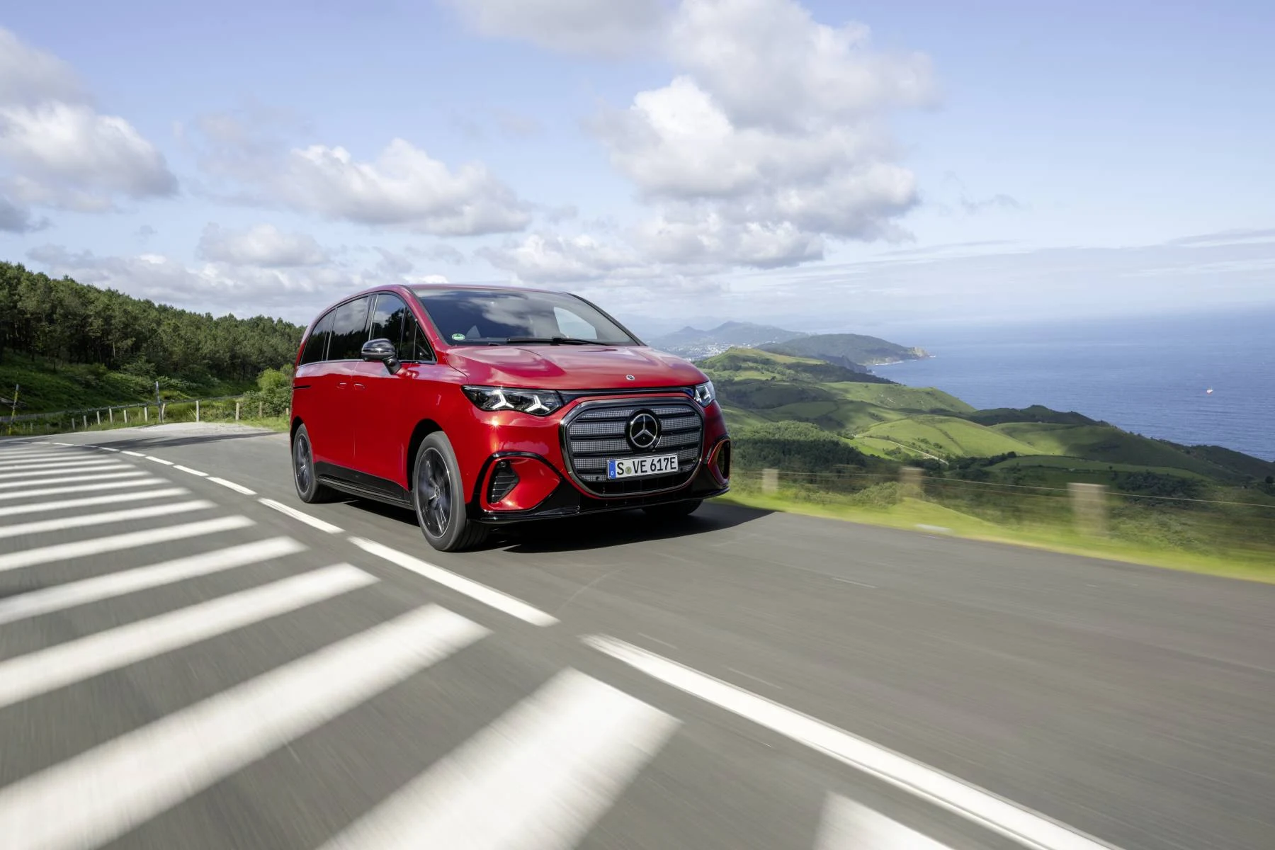 Červený Mercedes-Benz VLE v jízdě po silnici v kopcovité krajině
