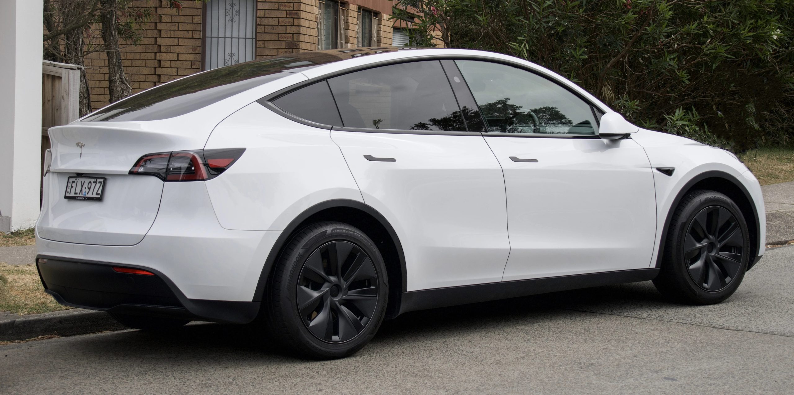 Bílá Tesla Model Y zaparkovaná u chodníku