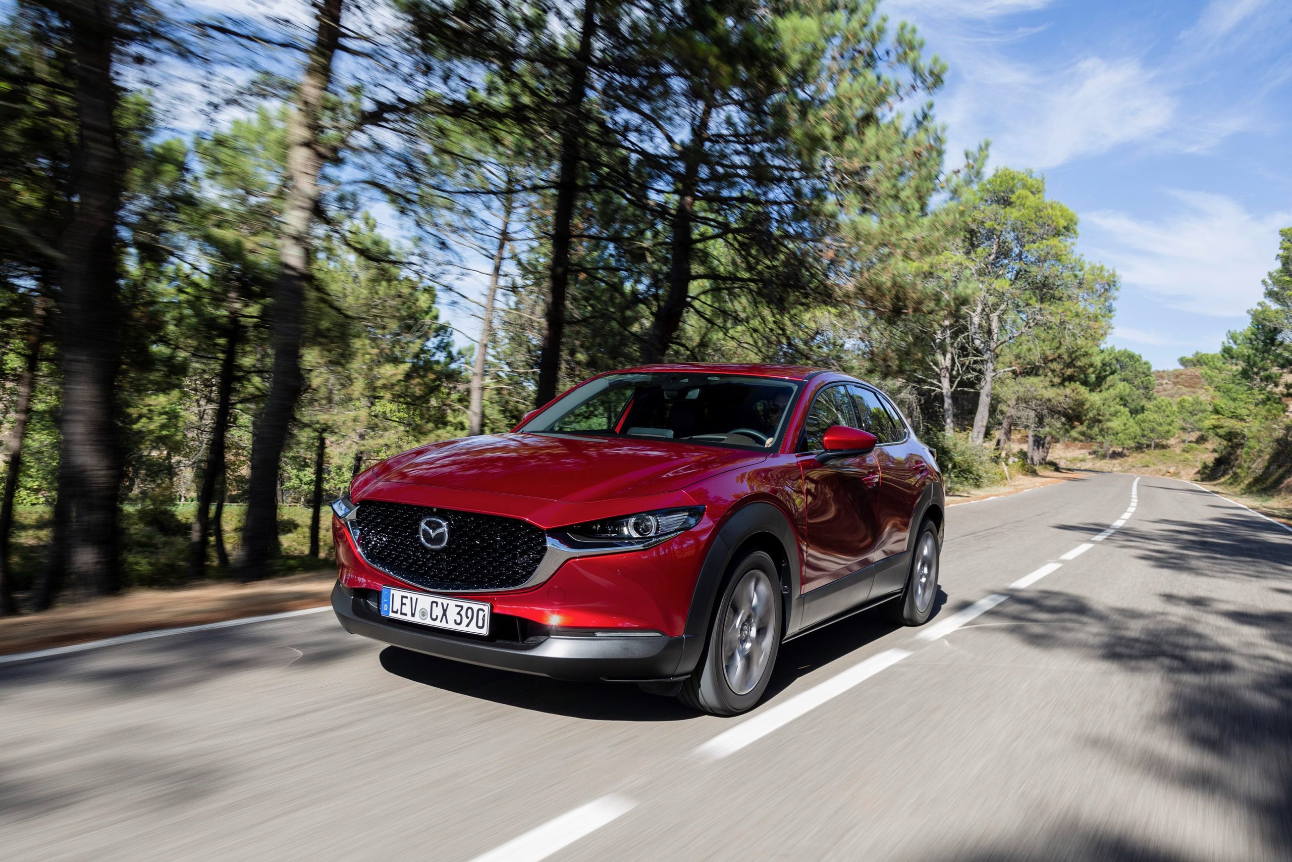 Červená Mazda CX-30 při jízdě na lesní silnici