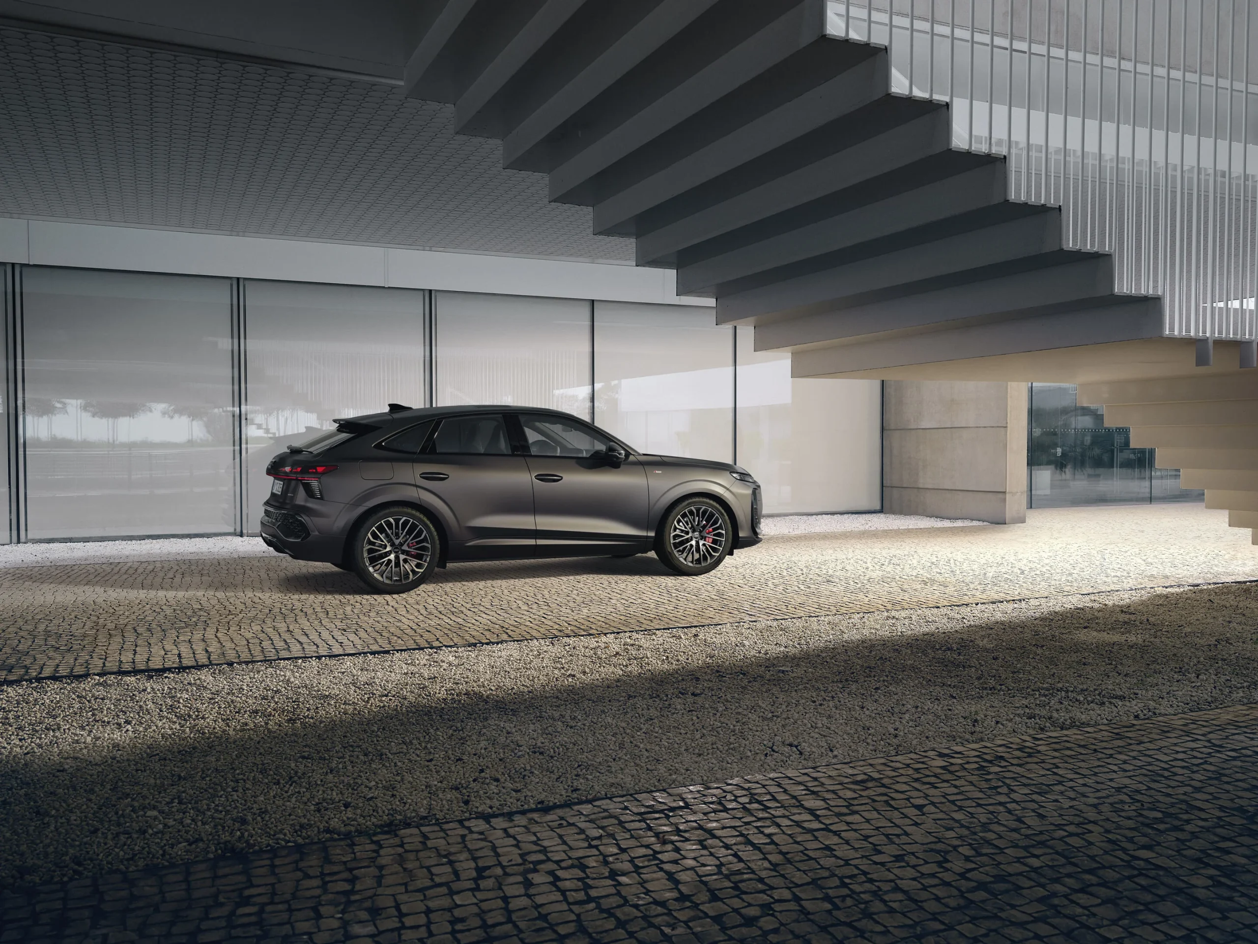 Audi Q3 Sportback z boku a šikmo zezadu před moderní budovou