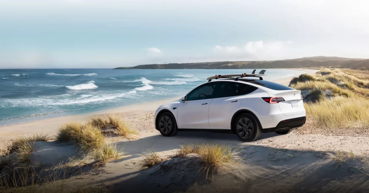 Bílý Tesla Model Y na pláži, boční záběr celého vozu
