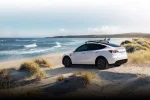 Bílý Tesla Model Y na pláži, boční záběr celého vozu