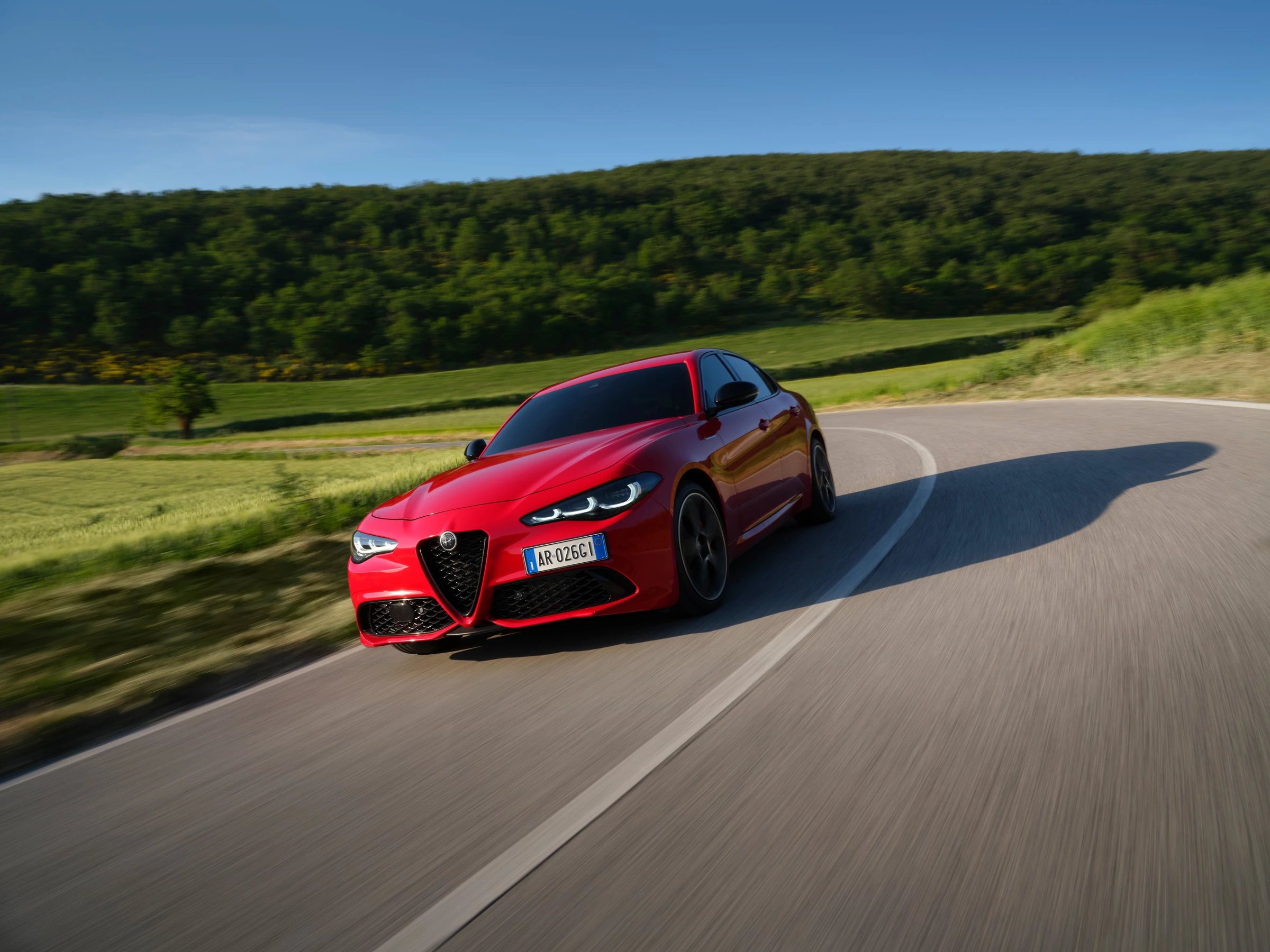 Modernizovaná červená Alfa Romeo Giulia z předního bočního pohledu při jízdě