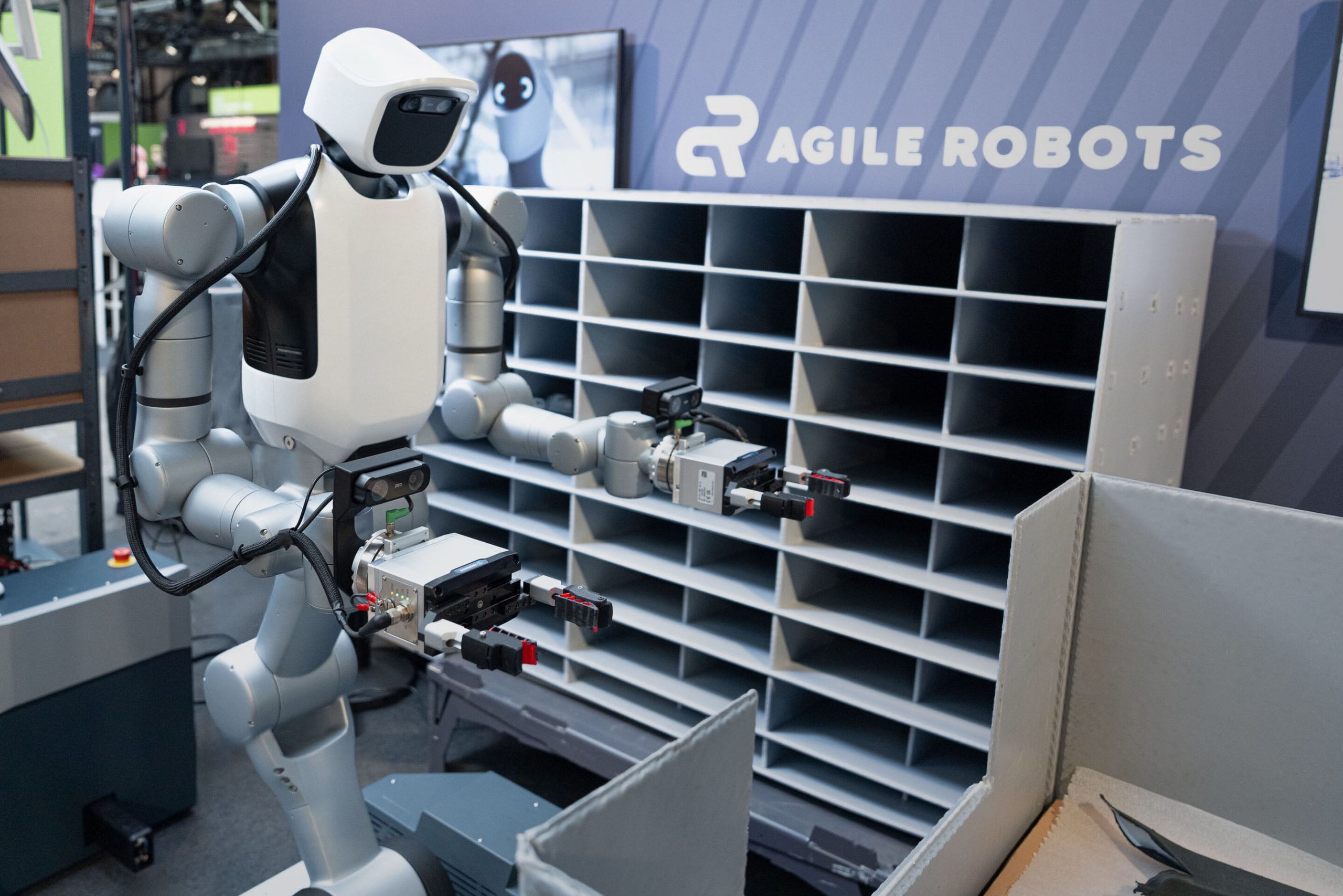 Humanoidní robot Agile Robots u přihrádkového regálu a přepravního boxu