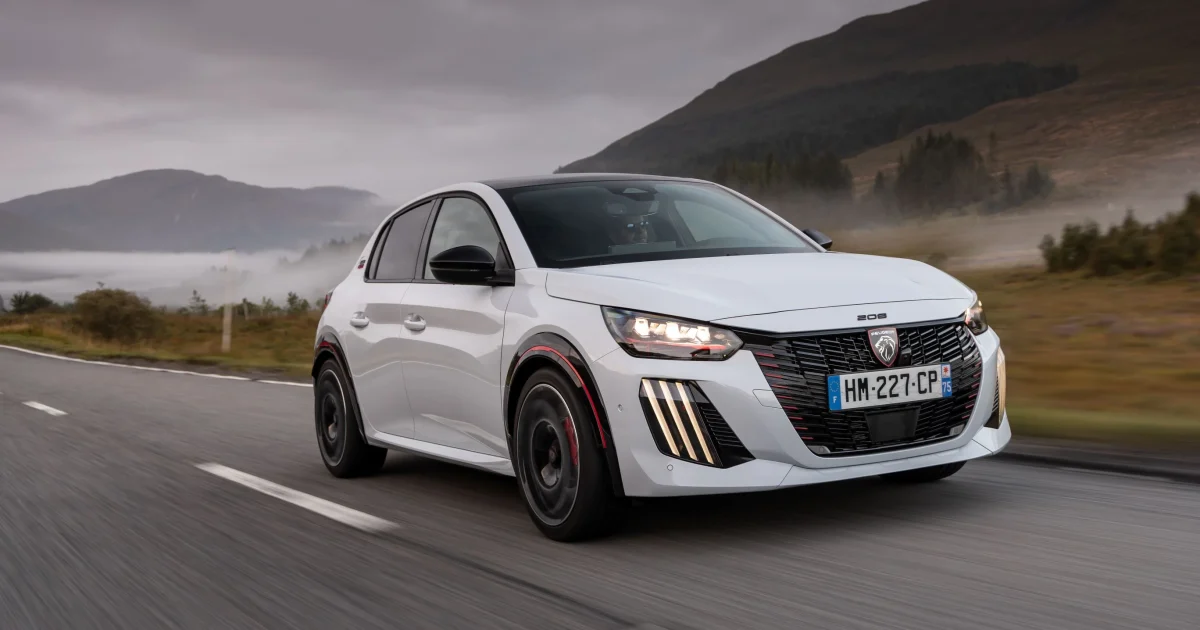 Peugeot E-208 GTi v bílé barvě při jízdě, pohled zepředu