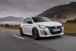 Peugeot E-208 GTi v bílé barvě při jízdě, pohled zepředu