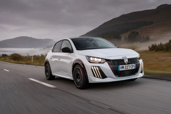 Peugeot E-208 GTi v bílé barvě při jízdě, pohled zepředu